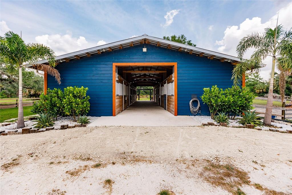 A blue barn with a central breezeway stands between two palm trees on a gravel lot — 9325 SW LIPE ROAD, ARCADIA, FL