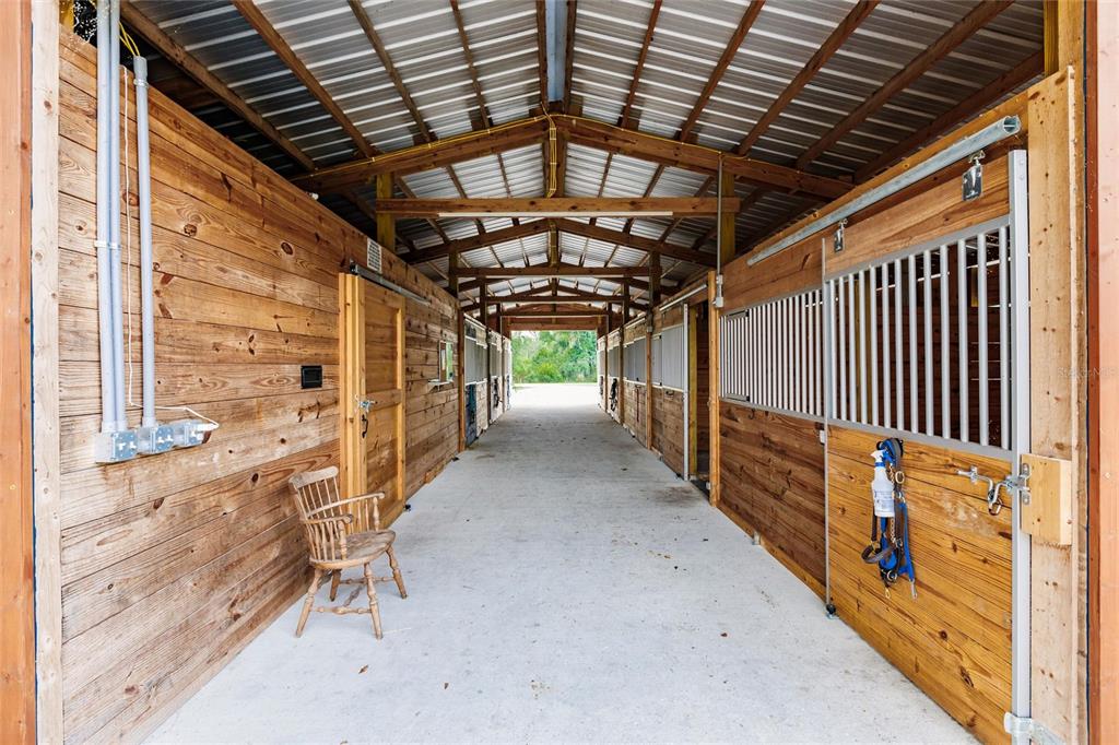 A view down the center aisle of a wooden horse barn with multiple stalls — 9325 SW LIPE ROAD, ARCADIA, FL