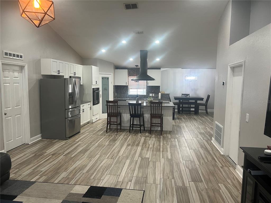 A kitchen with white cabinets, a central island with bar stools, and wood-look tile flooring — 5091 PLYMOUTH TURTLE CIRCLE, ST CLOUD, FL