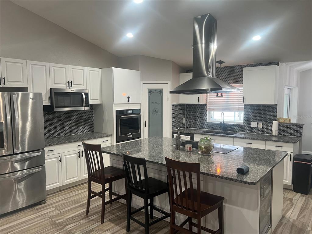 A kitchen features white cabinets, granite countertops, a large island with seating, and stainless appliances — 5091 PLYMOUTH TURTLE CIRCLE, ST CLOUD, FL