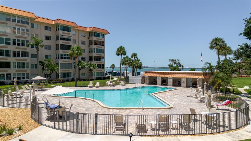A multi-story apartment building overlooks a swimming pool with a surrounding patio and fence — 632 EDGEWATER DRIVE UNIT 238, DUNEDIN, FL