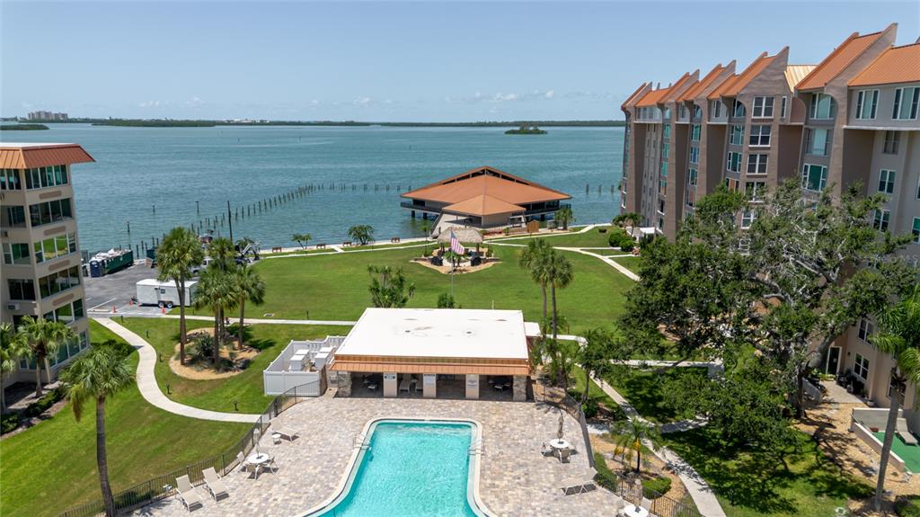 An aerial view shows a swimming pool, a grassy lawn, and buildings beside a bay — 632 EDGEWATER DRIVE UNIT 238, DUNEDIN, FL