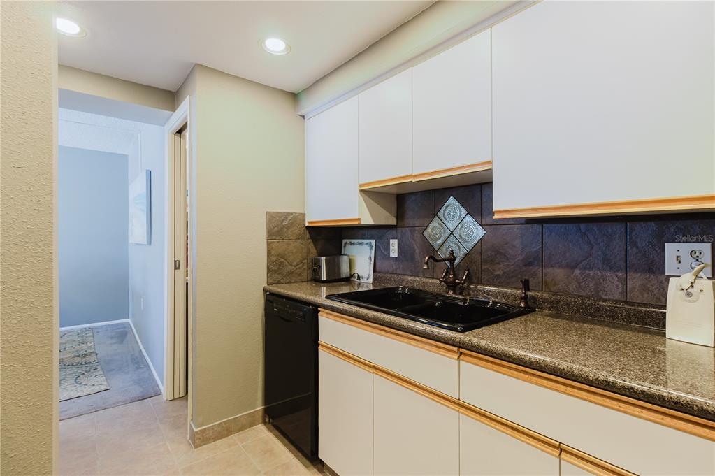 A kitchen features white cabinets, dark countertops, a black sink, and a tiled backsplash — 632 EDGEWATER DRIVE UNIT 238, DUNEDIN, FL