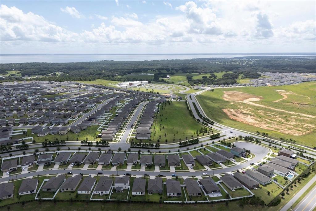 An aerial view shows a suburban residential neighborhood with rows of houses and nearby fields — 2098 HUNTSMAN RIDGE ROAD, MINNEOLA, FL