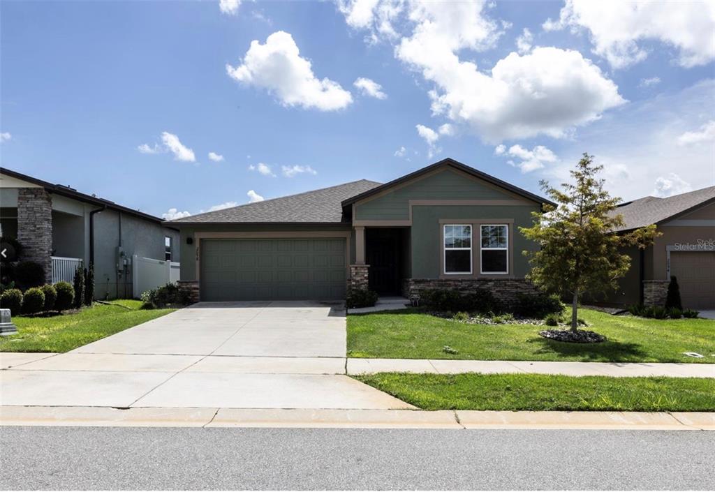 A single-story house with a green exterior, stone accents, a two-car garage, and a driveway — 2098 HUNTSMAN RIDGE ROAD, MINNEOLA, FL