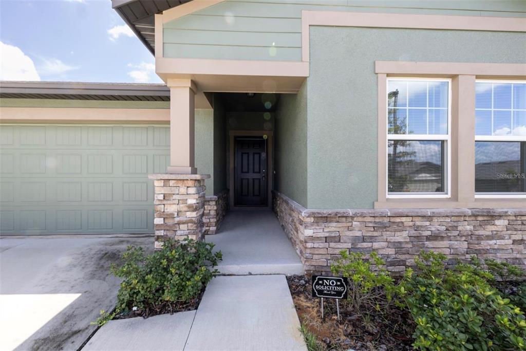 The exterior of a house features a stone-accented entryway, a dark front door, and garage — 2098 HUNTSMAN RIDGE ROAD, MINNEOLA, FL