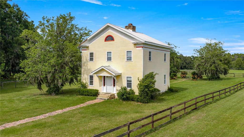 A two-story yellow farmhouse with a metal roof stands in a grassy, fenced-in field — 13939 N US HIGHWAY 441 UNIT (yellow house), CITRA, FL
