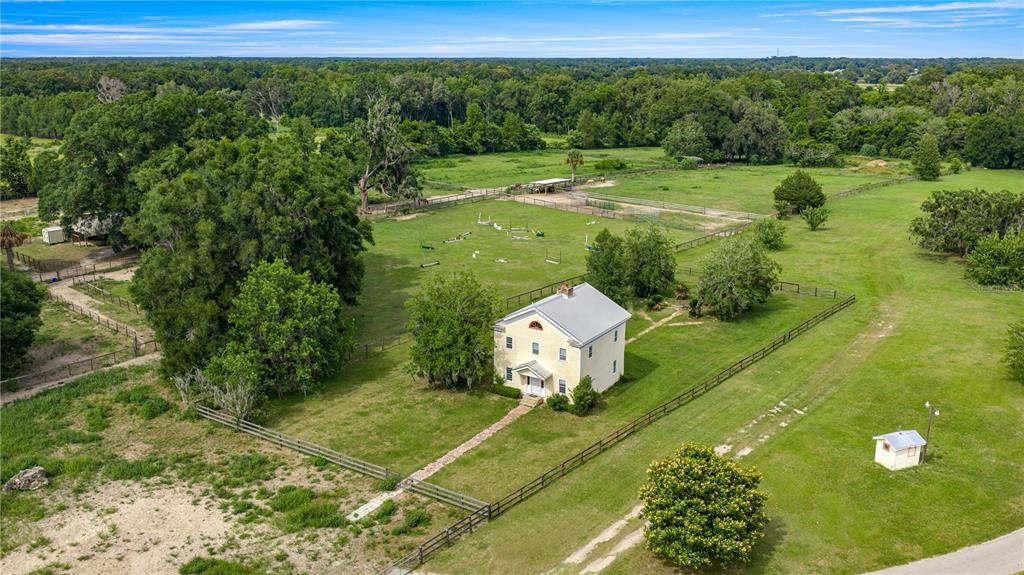 An aerial view shows a two-story house situated on a large, fenced rural property — 13939 N US HIGHWAY 441 UNIT (yellow house), CITRA, FL