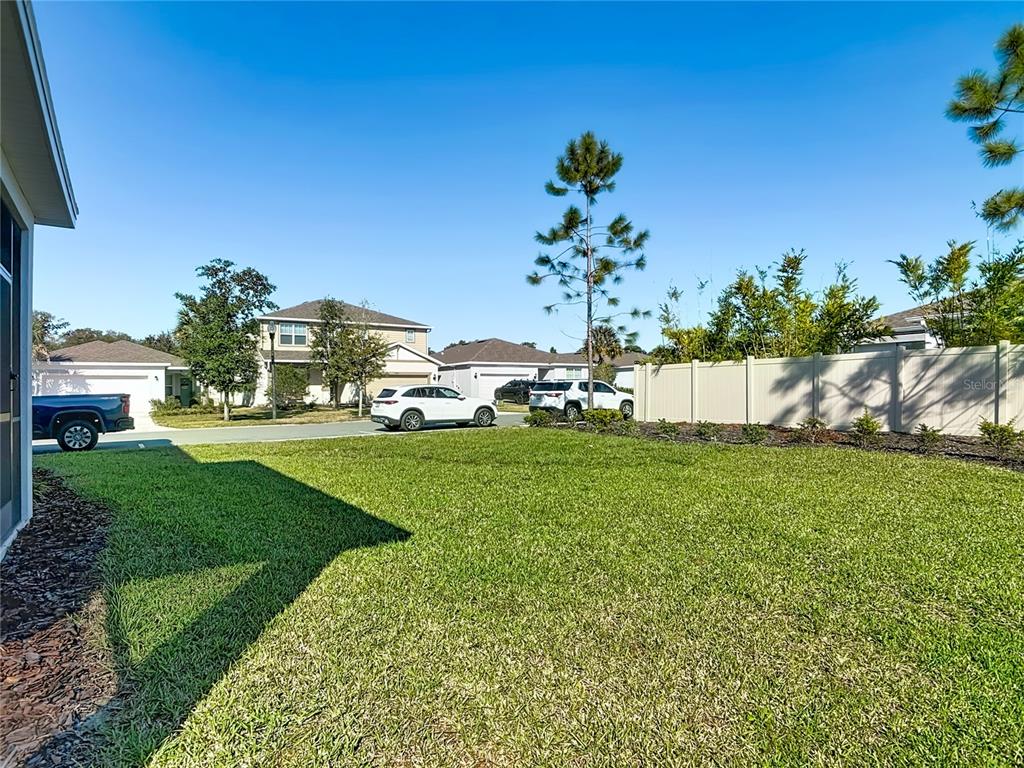 A grassy backyard features a white vinyl fence and a view of neighboring suburban houses — 2248 CANOPY TERRACE BOULEVARD, DELAND, FL