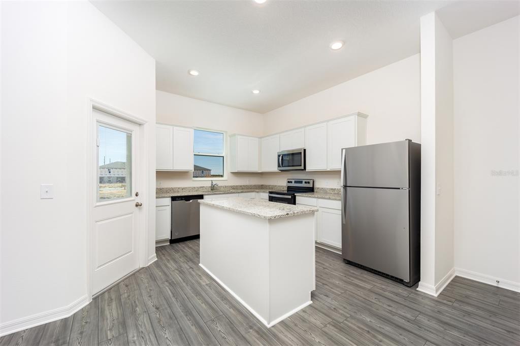 A kitchen with white cabinets, granite countertops, stainless steel appliances, and gray wood-look flooring — 691 POPPY LANE, DUNDEE, FL