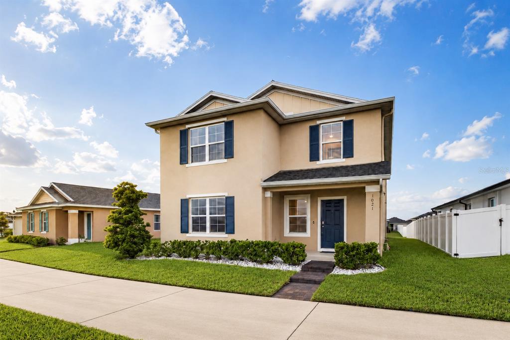 A two-story tan house with blue shutters and a dark front door under a blue sky — 1021 SILVERBELL TRAIL, ST CLOUD, FL
