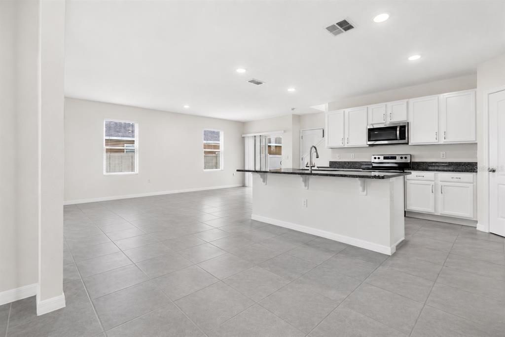 An open-concept kitchen and living area features white cabinetry, granite countertops, and gray tile flooring — 1021 SILVERBELL TRAIL, ST CLOUD, FL