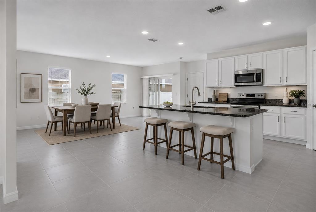 A bright, open-concept kitchen and dining area featuring white cabinetry, a granite-topped island, and tile flooring — 1021 SILVERBELL TRAIL, ST CLOUD, FL