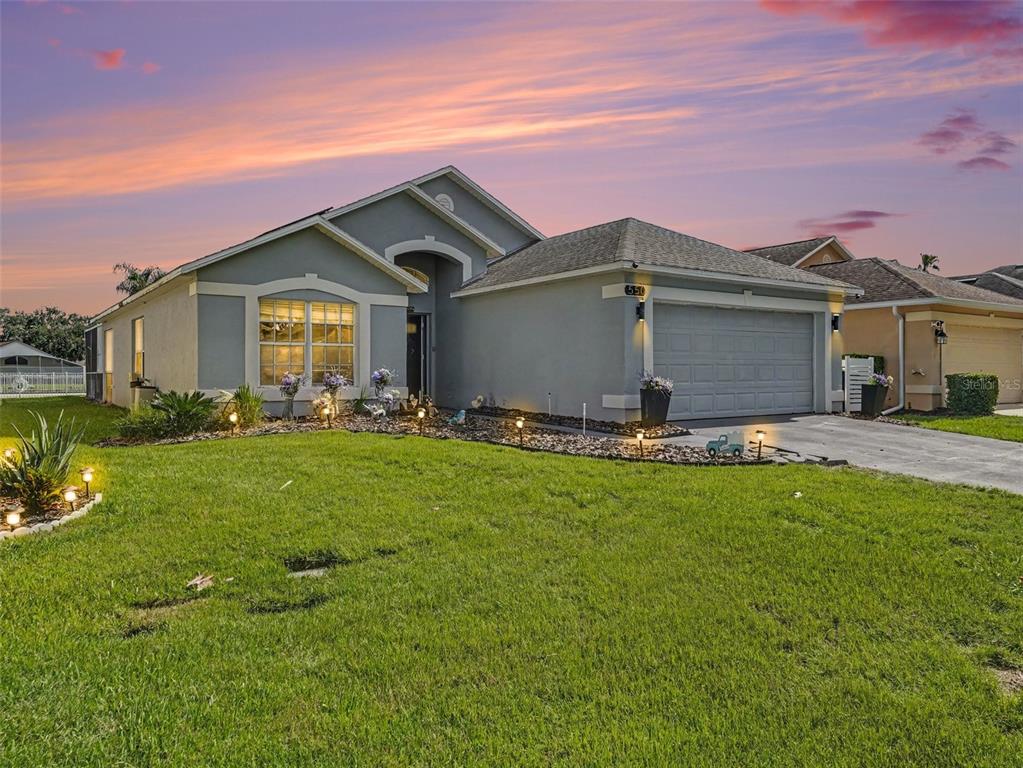 A single-story suburban house with a gray stucco exterior, a two-car garage, and a lawn — 550 BUCKINGHAM CIRCLE, DAVENPORT, FL