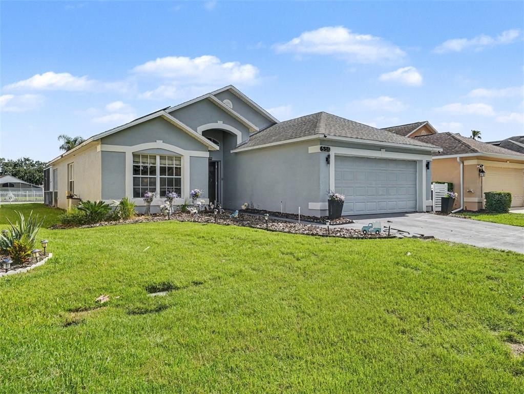 A single-story suburban house with a gray stucco exterior, a two-car garage, and a lawn — 550 BUCKINGHAM CIRCLE, DAVENPORT, FL