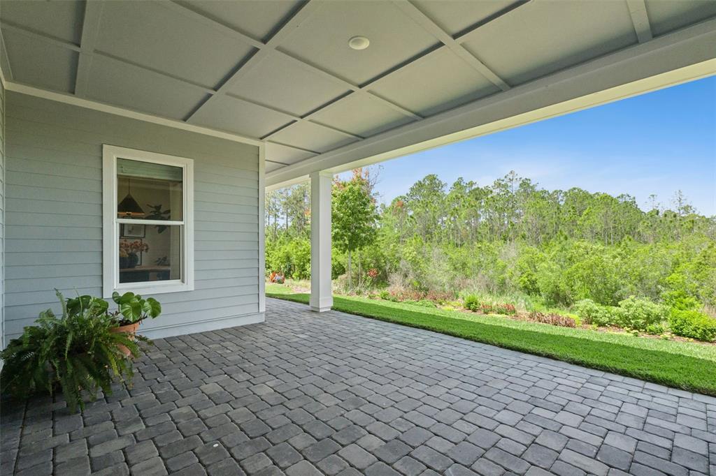 A covered patio with gray pavers overlooks a grassy lawn and a dense forest — 6410 TRAILBLAZE BEND, ST CLOUD, FL