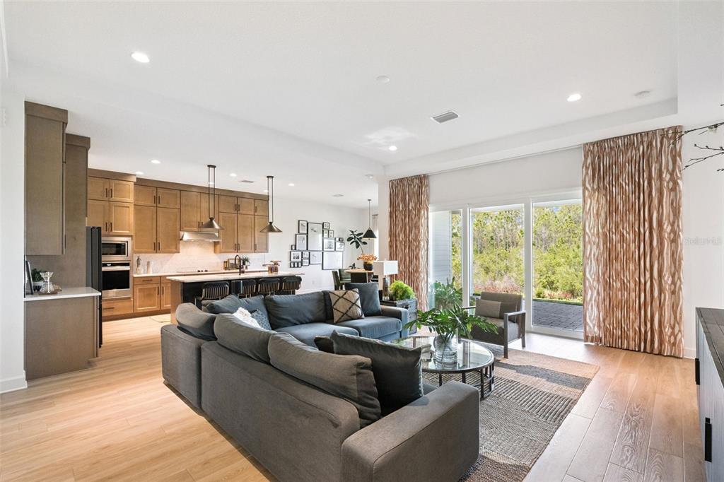 An open-concept living room and kitchen with wood flooring, a gray sectional, and large windows — 6410 TRAILBLAZE BEND, ST CLOUD, FL
