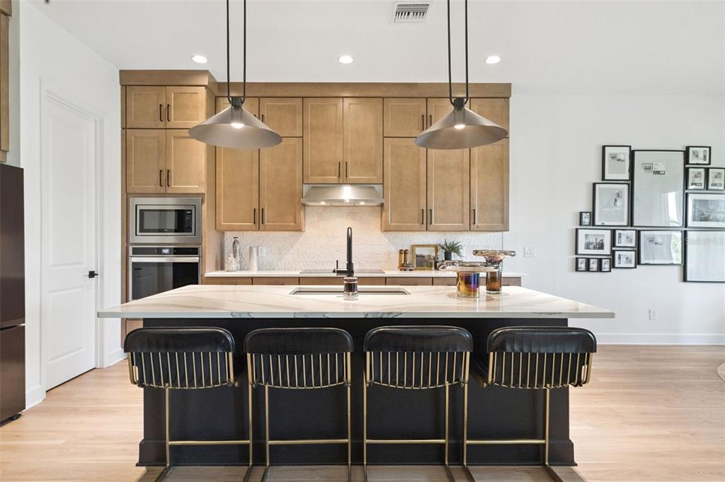 A kitchen features a dark island with four stools, light wood cabinets, and pendant lighting — 6410 TRAILBLAZE BEND, ST CLOUD, FL
