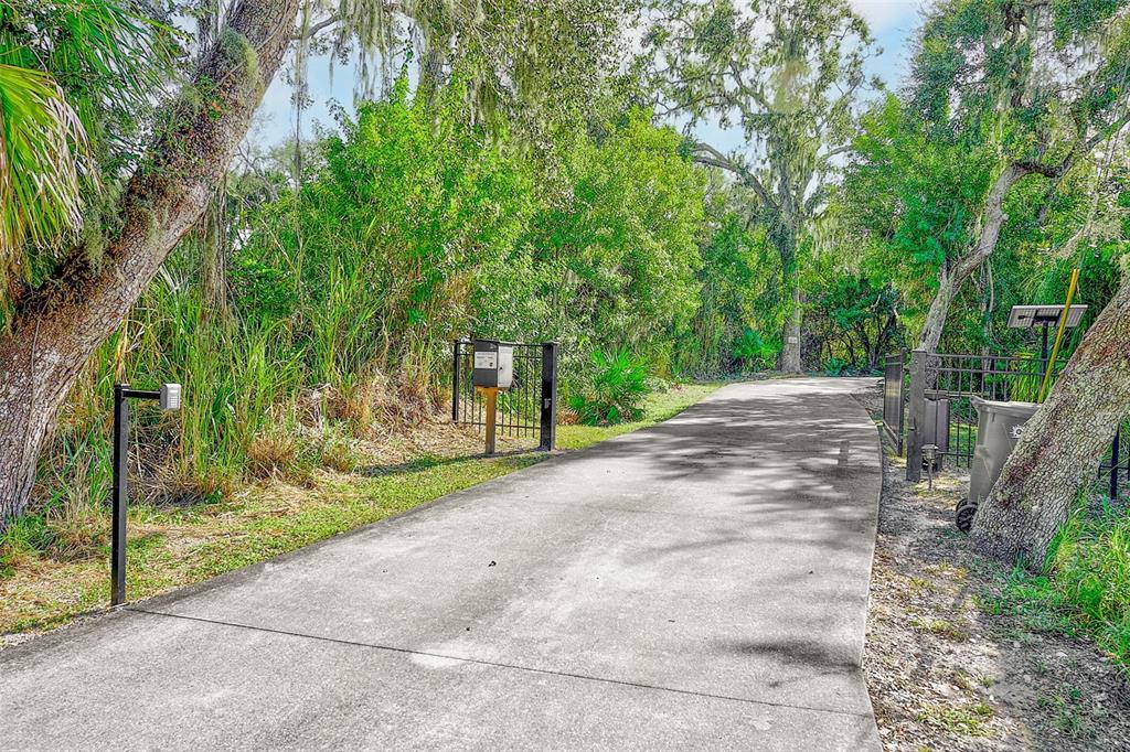 A concrete driveway leads toward a gated entrance surrounded by lush trees and vegetation — 3410 26TH AVENUE E, BRADENTON, FL