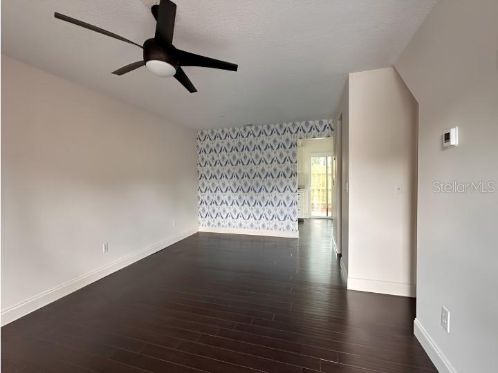 A living room with dark wood floors, a ceiling fan, and a patterned accent wall — 7413 BELLE RIVER COURT UNIT 3, WINTER PARK, FL