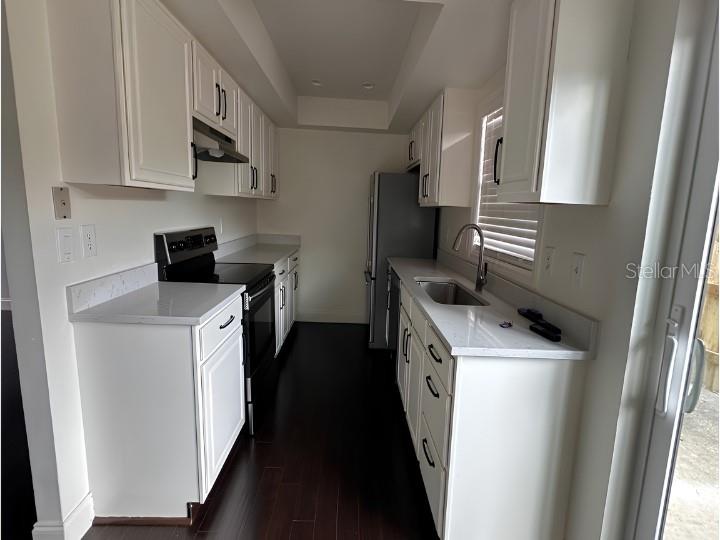 A galley kitchen features white cabinets, dark wood floors, and stainless steel appliances — 7413 BELLE RIVER COURT UNIT 3, WINTER PARK, FL