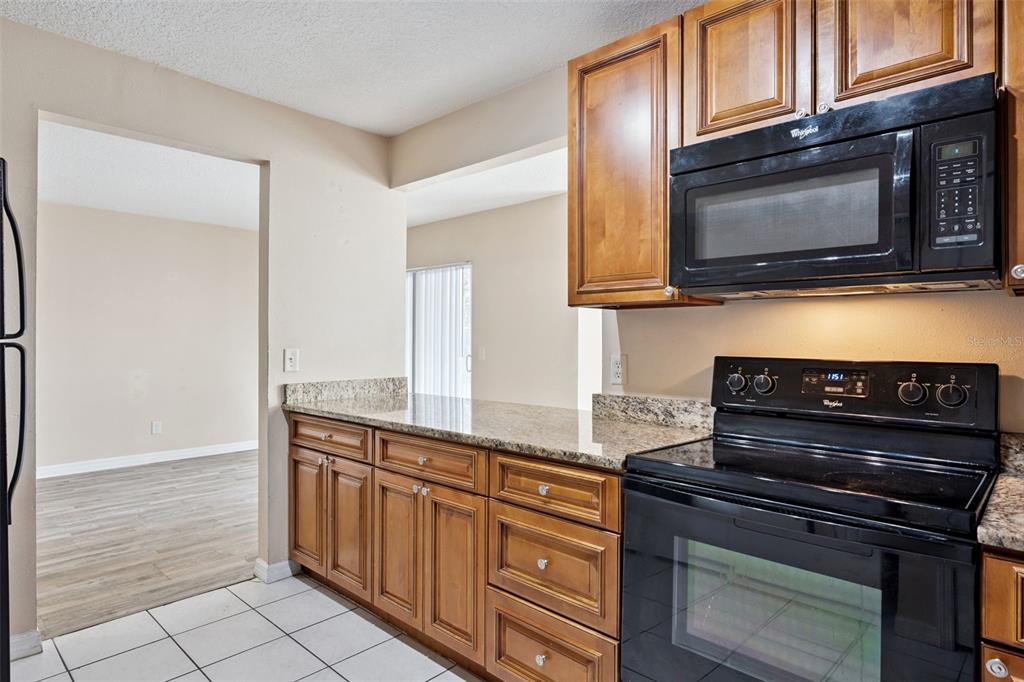 A kitchen features wood cabinets, granite countertops, black appliances, and white tile flooring — 2401 BARLEY CLUB COURT UNIT 2, ORLANDO, FL