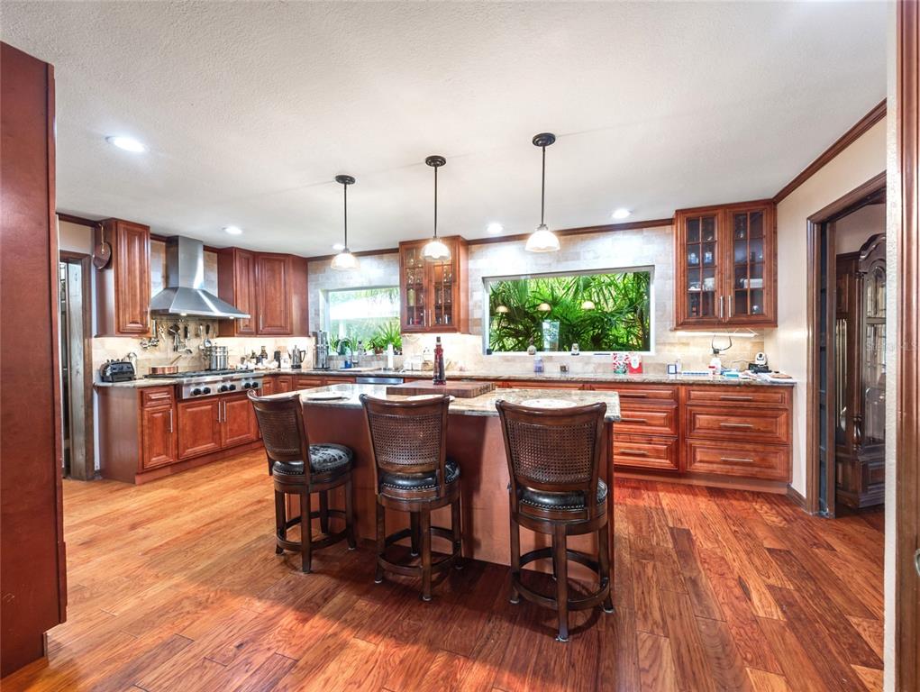 A kitchen features wood cabinetry, a central island with three stools, and hardwood flooring — 15733 TOWER VIEW DRIVE, CLERMONT, FL
