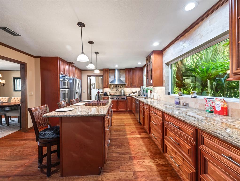 A kitchen features wood cabinets, granite countertops, a center island, and a large window view — 15733 TOWER VIEW DRIVE, CLERMONT, FL