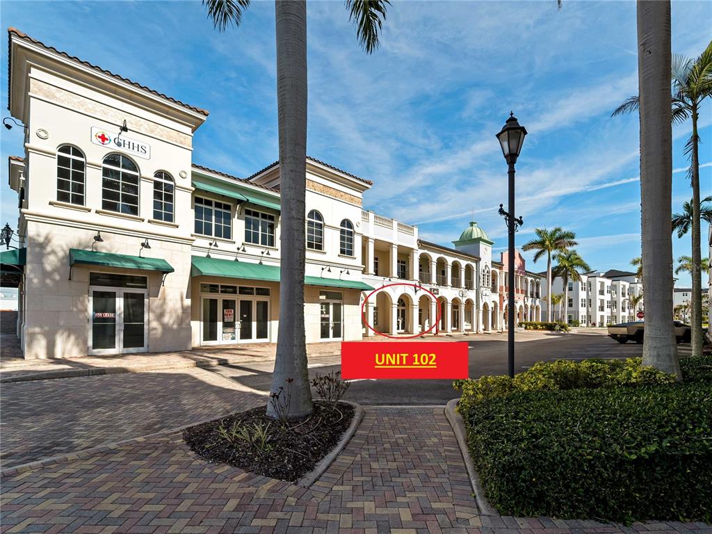 A multi-story commercial building with arched walkways and a paved courtyard under a blue sky — 3976 DESTINATION DRIVE UNIT 102, OSPREY, FL