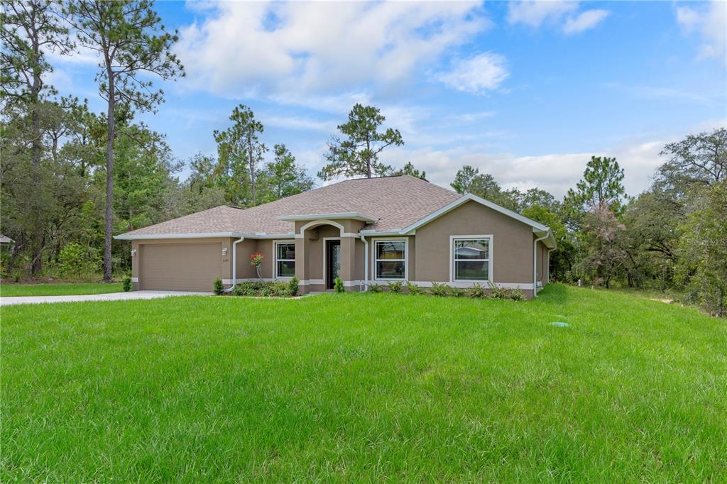 A single-story tan stucco house with a two-car garage sits on a grassy lot — 13048 KITTIWAKE ROAD, WEEKI WACHEE, FL