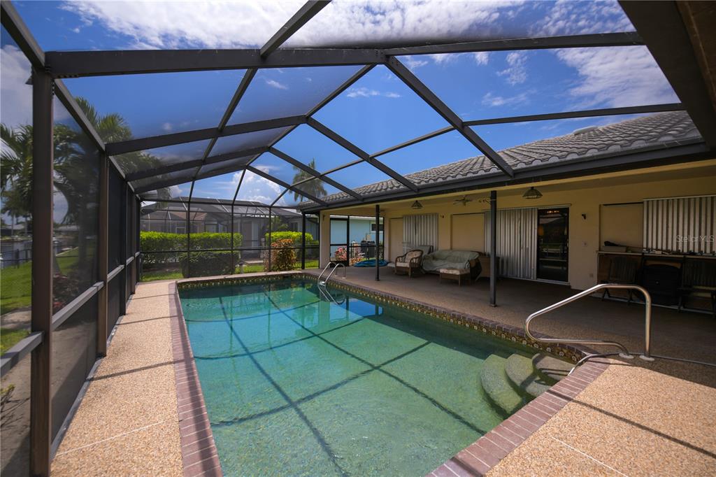 A screened-in swimming pool with a concrete deck and a covered patio area — 1205 VIA TRIPOLI, PUNTA GORDA, FL