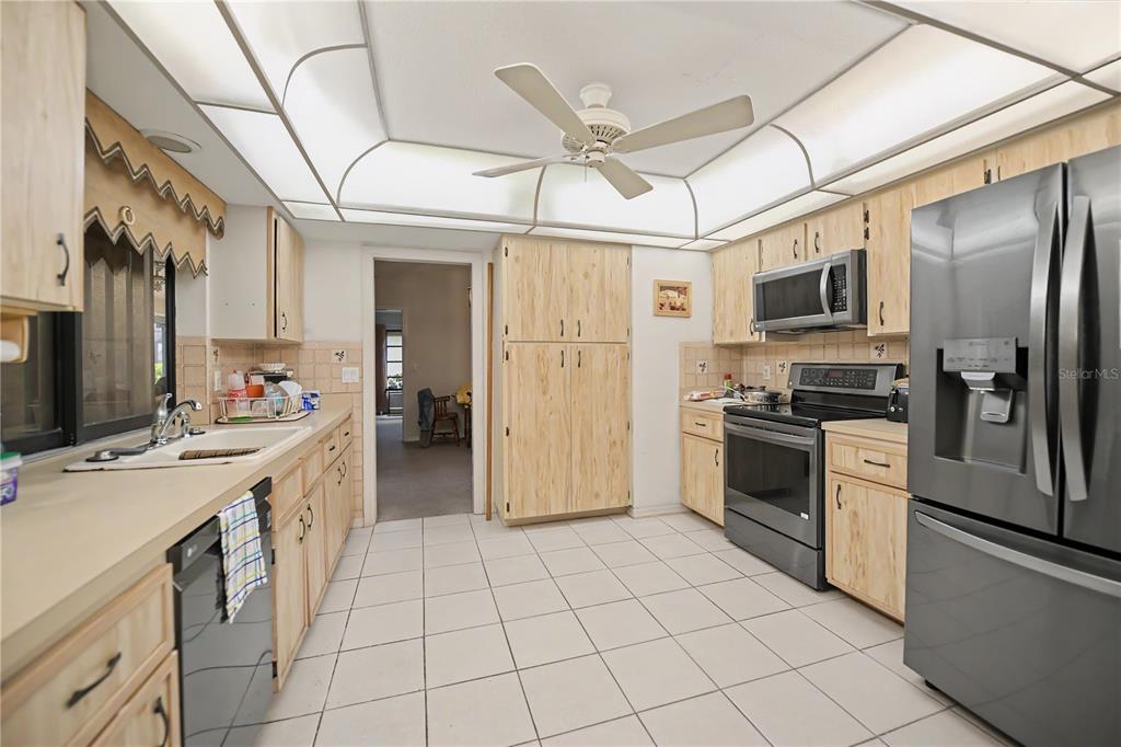 A kitchen with light wood cabinets, stainless steel appliances, white tile flooring, and a ceiling fan — 1205 VIA TRIPOLI, PUNTA GORDA, FL