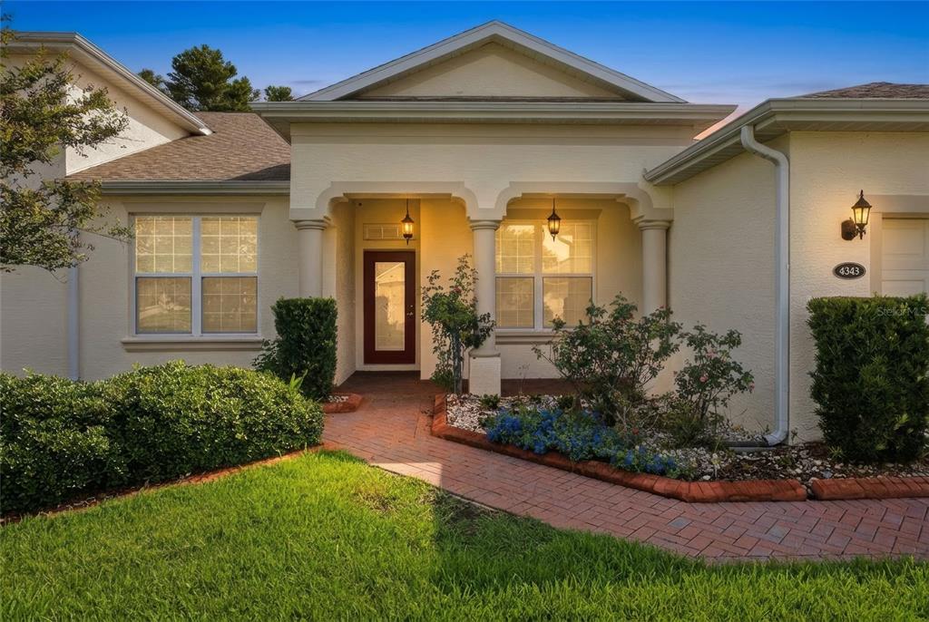 A beige stucco house features a brick walkway leading to a covered front entryway — 4343 HERITAGE TRAIL, LEESBURG, FL