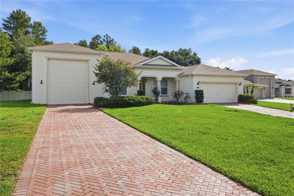 A single-story house features a brick driveway, a tall garage door, and a standard garage — 4343 HERITAGE TRAIL, LEESBURG, FL