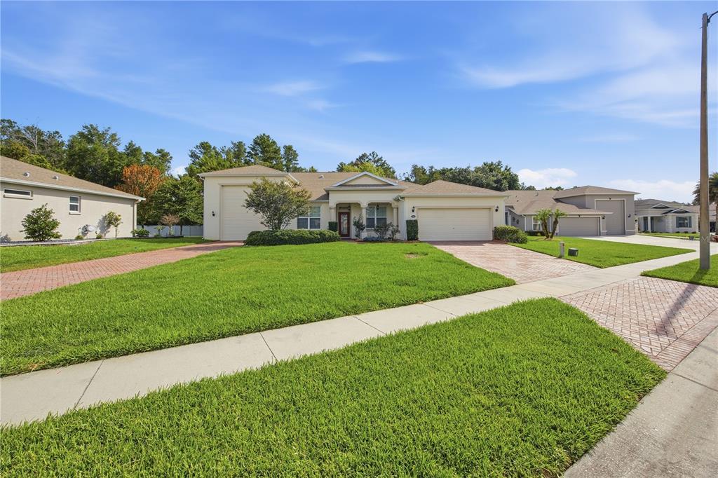 A single-story house with a beige exterior, a two-car garage, and a brick-paved driveway — 4343 HERITAGE TRAIL, LEESBURG, FL