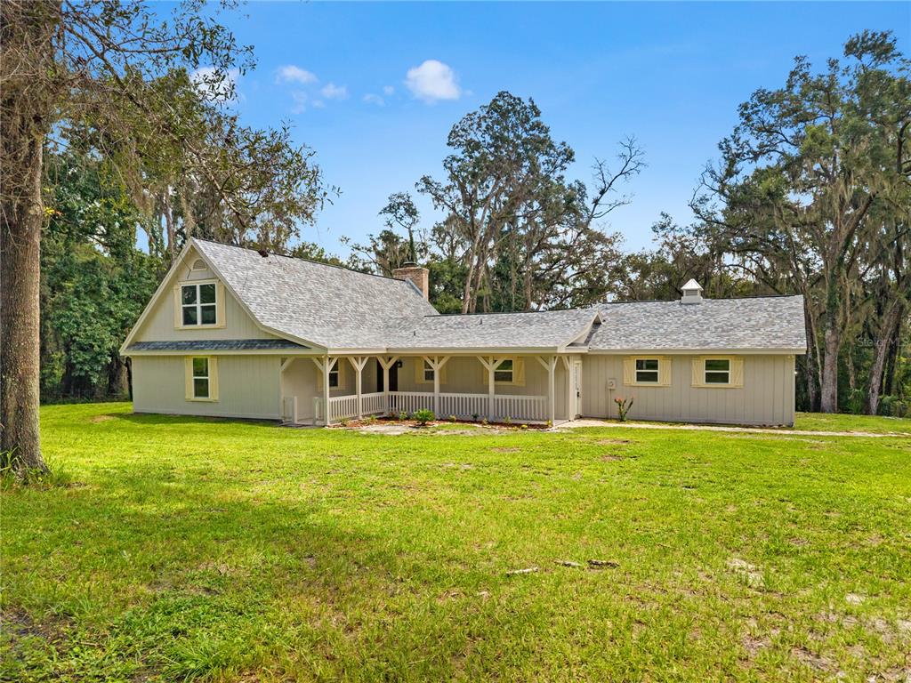 A light gray house with a wrap-around porch sits on a grassy lawn among trees — 3270 ENDSLEY ROAD, BROOKSVILLE, FL