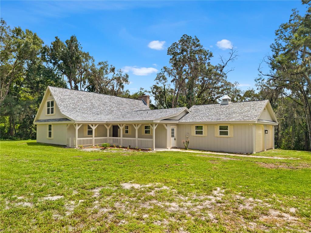 A light-colored house with a wrap-around porch and a two-car garage sits on grass — 3270 ENDSLEY ROAD, BROOKSVILLE, FL