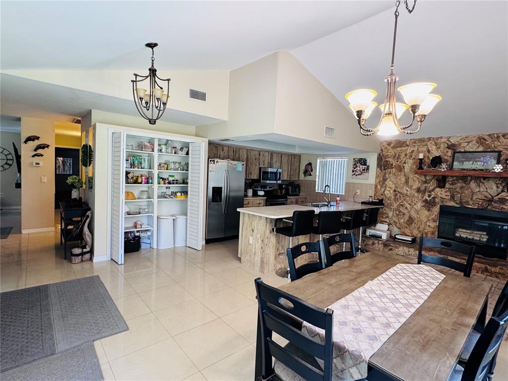An open-concept kitchen and dining area features a stone fireplace, tile flooring, and wood cabinetry — 7590 N CAESAR POINT, DUNNELLON, FL