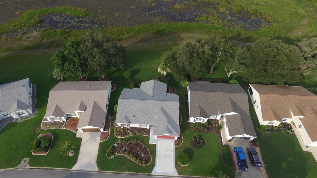 An aerial view shows four suburban houses with driveways and lawns bordering a grassy pond — 4755 TARA VIEW ROAD, LEESBURG, FL