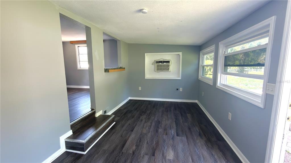 A room with dark wood-look flooring, light blue walls, two windows, and a wall-mounted air conditioner — 11772 SE 99TH TERRACE, BELLEVIEW, FL