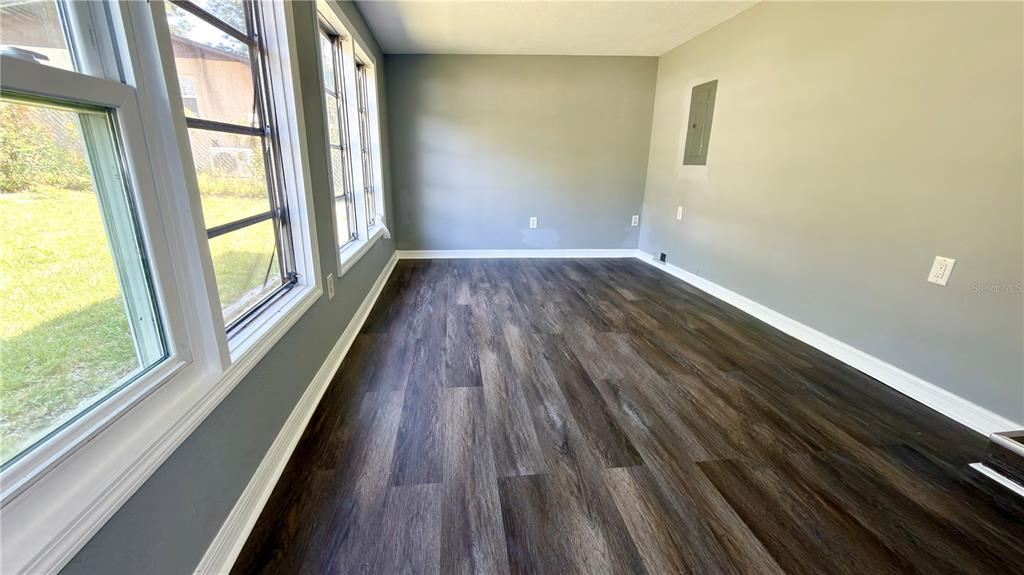An empty room features dark wood-look flooring, gray walls, and large windows along one side — 11772 SE 99TH TERRACE, BELLEVIEW, FL