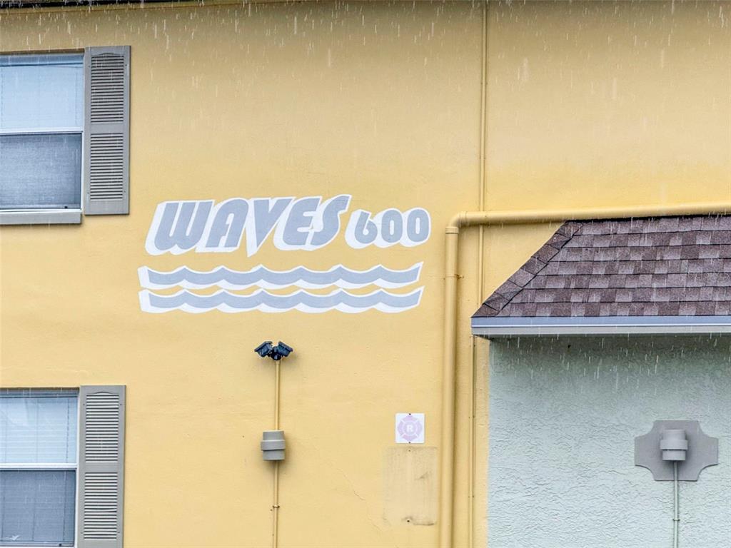 The exterior of a yellow building features a sign reading WAVES 600 with wave graphics — 600 71ST AVENUE UNIT 18, ST PETE BEACH, FL