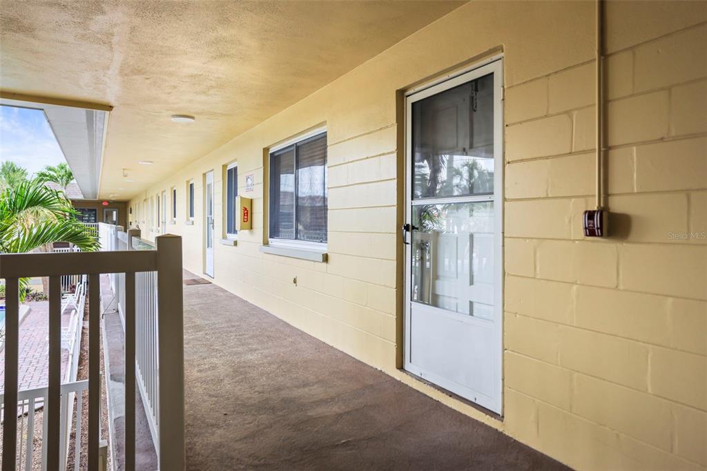 An outdoor walkway with yellow concrete block walls, a white screen door, and a railing — 600 71ST AVENUE UNIT 18, ST PETE BEACH, FL