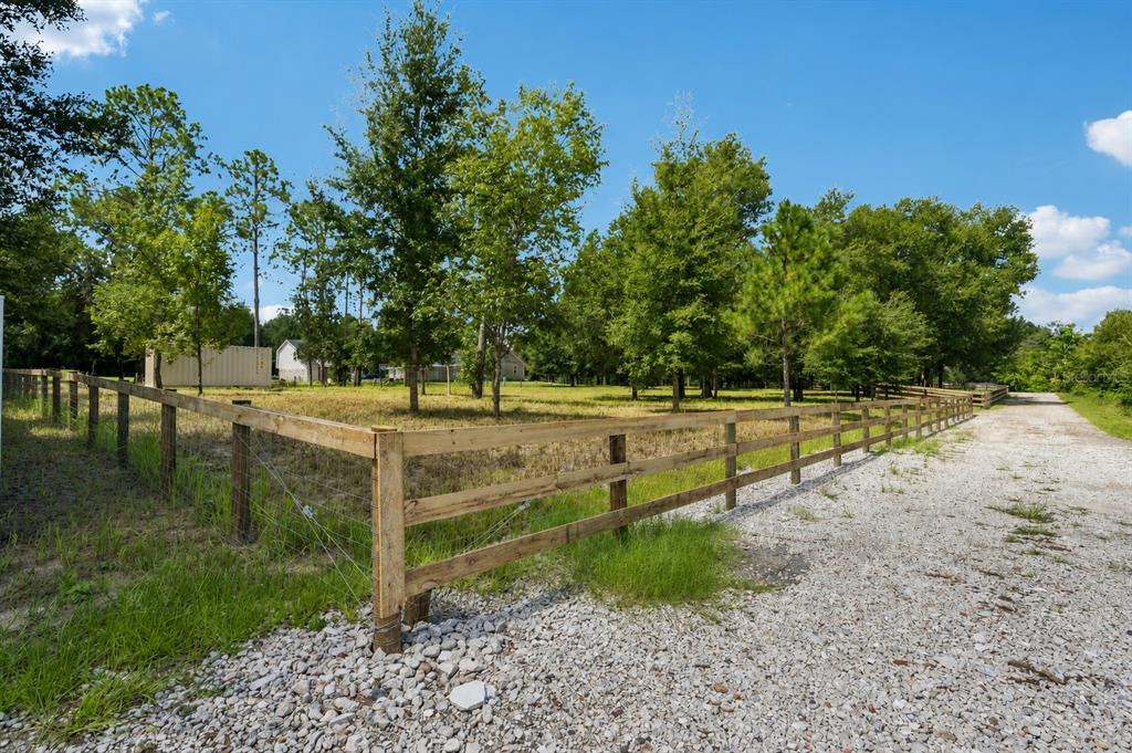 A wooden fence encloses a grassy lot with scattered trees next to a gravel driveway — 0 RAISER RD, DADE CITY, FL