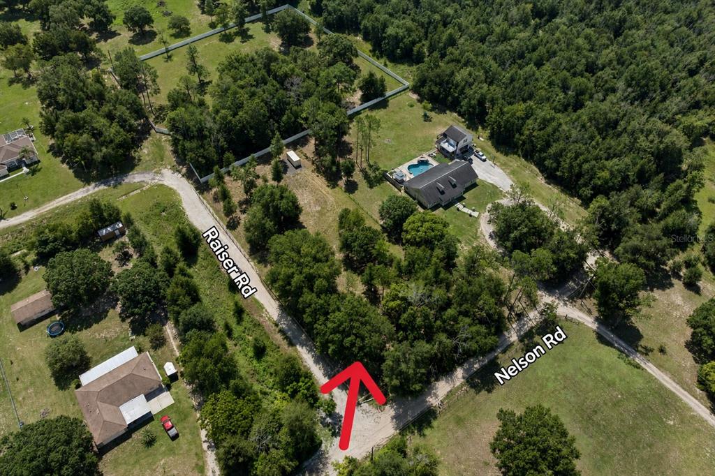 An aerial view shows a wooded residential lot at the intersection of two dirt roads — 0 RAISER RD, DADE CITY, FL
