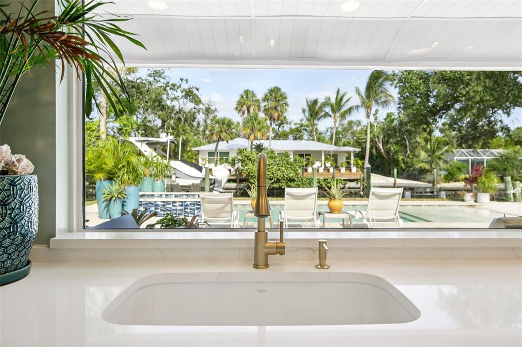 A kitchen sink with a gold faucet overlooks a patio, swimming pool, and canal — 613 BUTTONWOOD DRIVE, LONGBOAT KEY, FL