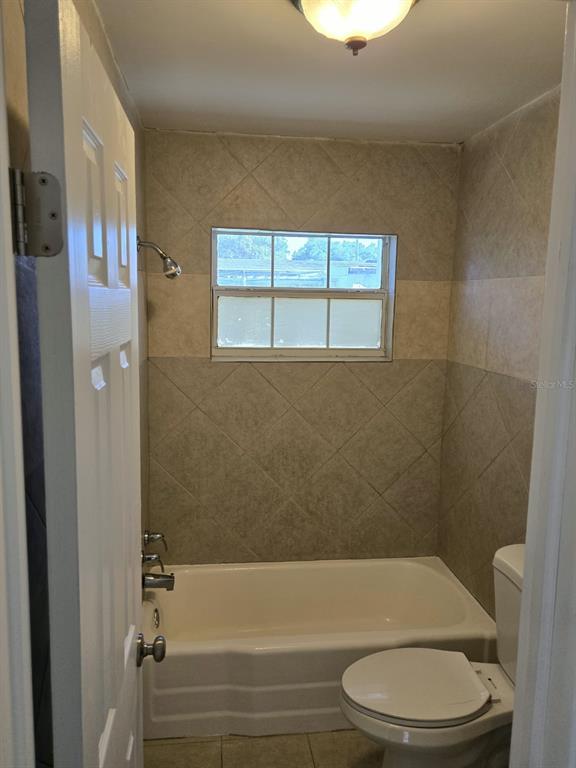 A bathroom features a white bathtub, a toilet, and beige tiled walls with a window — 5772 94TH AVENUE N, PINELLAS PARK, FL