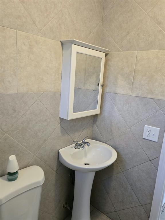 A bathroom features a pedestal sink, a white medicine cabinet, and light-colored diagonal wall tiles — 5772 94TH AVENUE N, PINELLAS PARK, FL