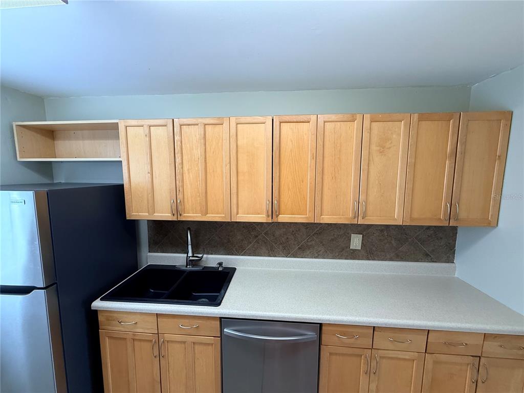 A kitchen features light wood cabinets, a black sink, and a stainless steel dishwasher — 6519 W NEWBERRY ROAD UNIT 305, GAINESVILLE, FL