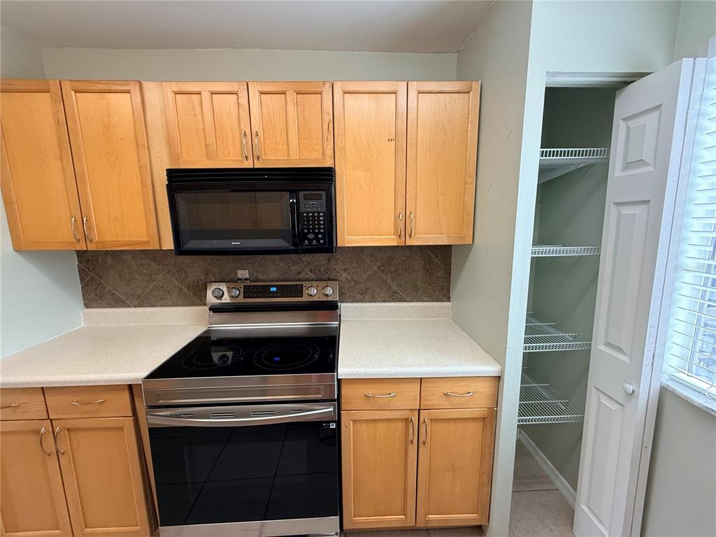A kitchen features light wood cabinets, a stainless steel stove, and an adjacent pantry closet — 6519 W NEWBERRY ROAD UNIT 305, GAINESVILLE, FL